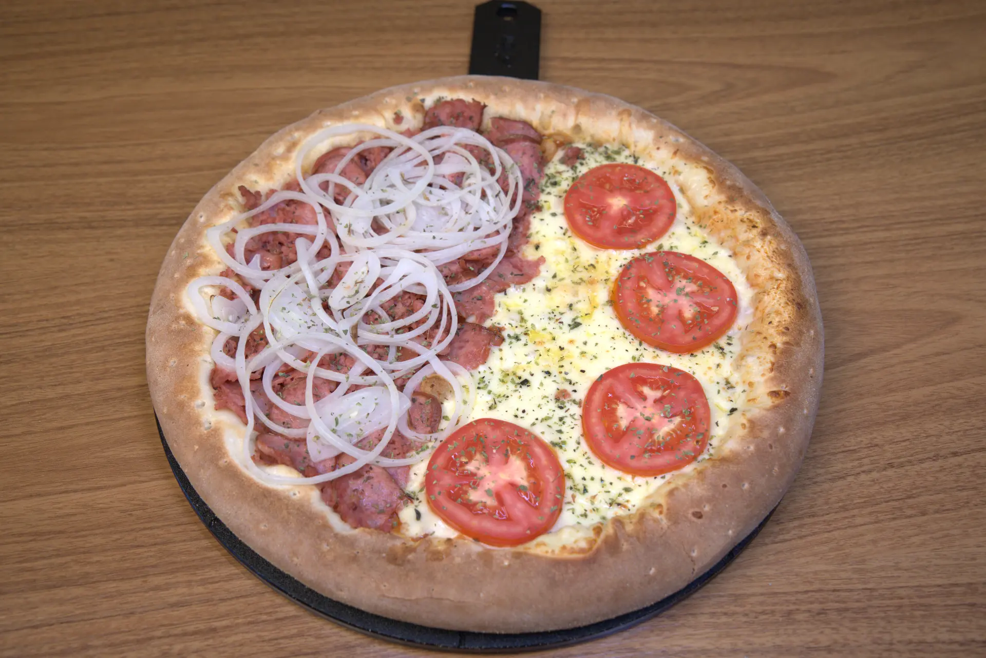 Pizza salgada metade calabresa e metade mussarela sobre tábua de madeira